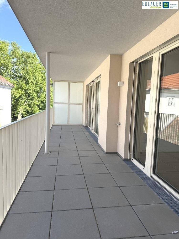 Geräumiger Balkon mit Fliesenboden und Zugang zu den Innenräumen, umgeben von Grün.