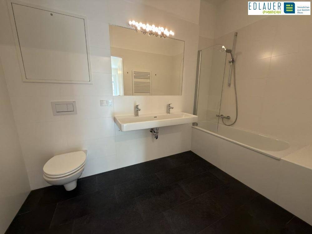 Modernes Badezimmer mit Doppelwaschbecken, Badewanne und Wand-WC, ausgestattet mit dunklen Bodenfliesen.