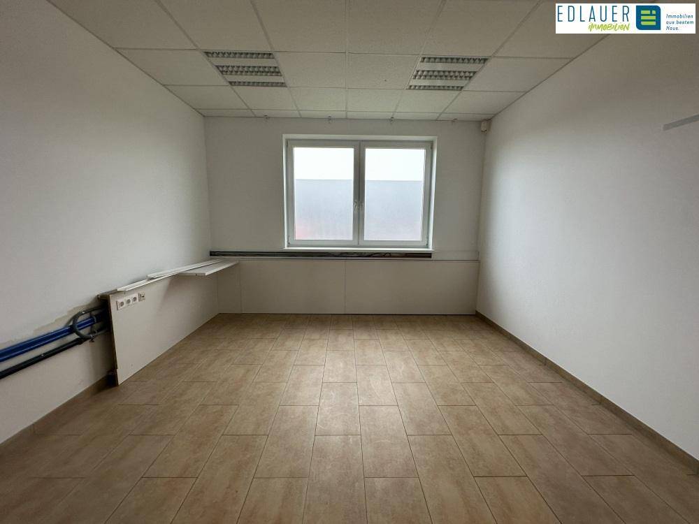 Schlichter Büroraum mit Fliesenboden, Fenster und Deckenbeleuchtung, ideal für konzentriertes Arbeiten.