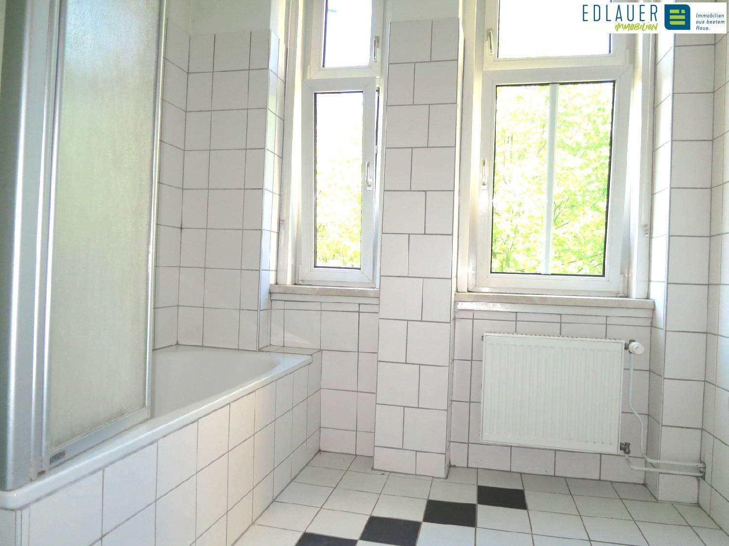 Badezimmer mit Badewanne, Duschabtrennung und zwei Fenstern für natürliche Belüftung.