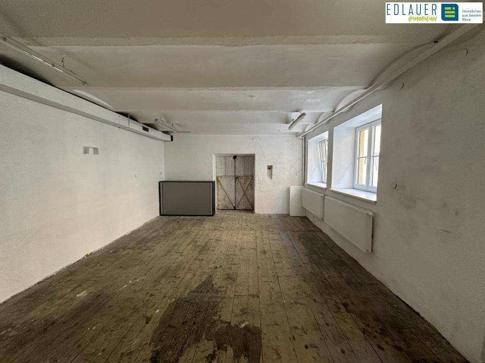Raum mit altem Holzdielenboden, sichtbaren Rohren und Fenstern, der Renovierungsbedarf aufweist.