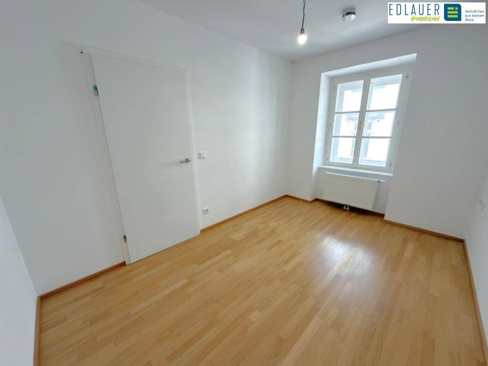 Ruhiges Zimmer mit Parkettboden und einem Fenster, ideal als Schlafzimmer oder Arbeitsbereich.