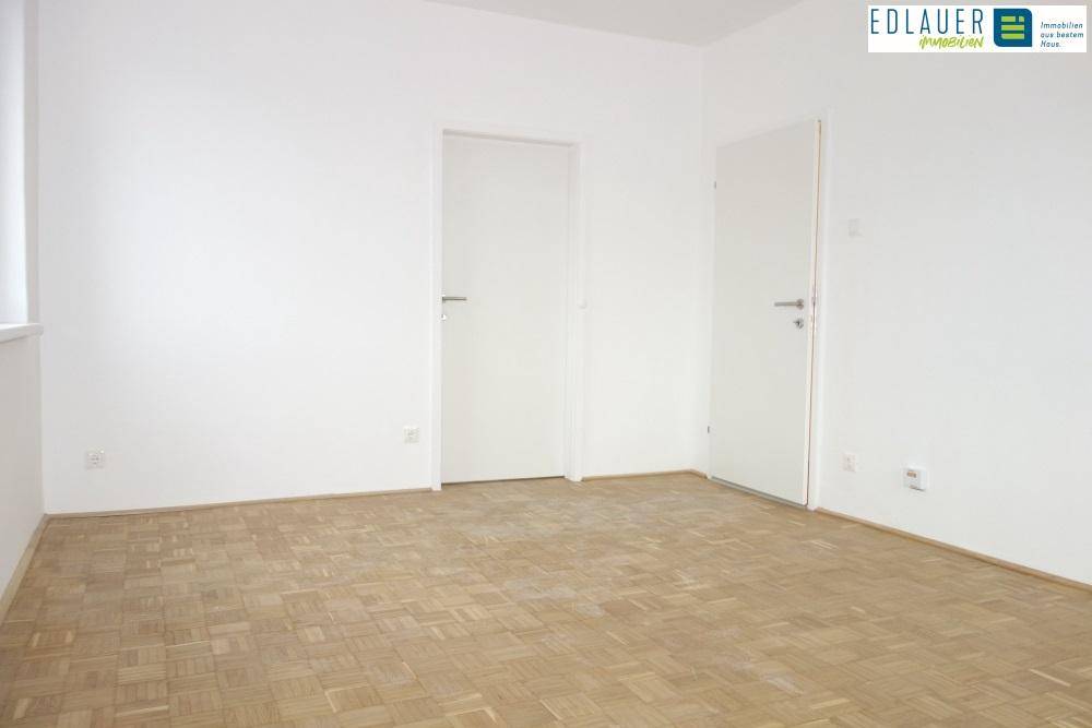 Leerer Raum mit Parkettboden, weißen Wänden und zwei weißen Innentüren.