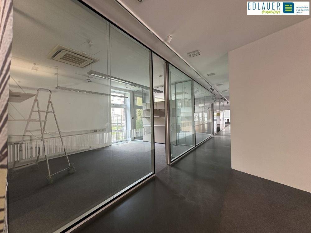 Langer Bürogang mit Glaswänden, Teppichboden und Blick in weitere Bürobereiche, die eine offene Gestaltung ermöglichen.