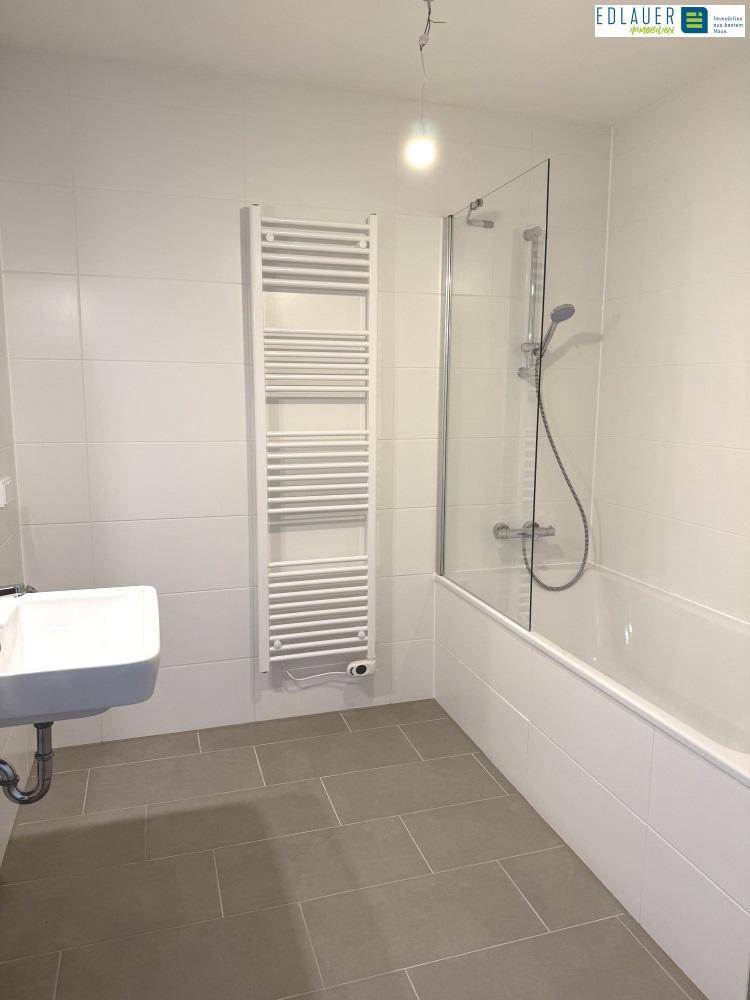 Modernes Badezimmer mit Badewanne, Duschabtrennung und beheiztem Handtuchhalter.
