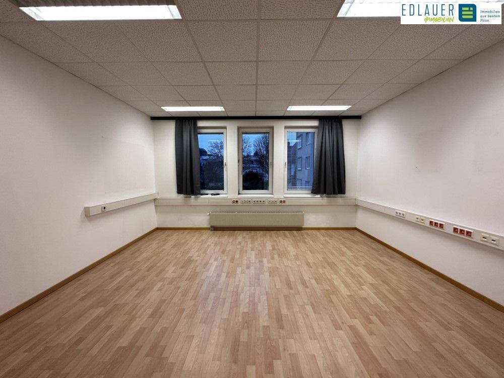 Heller Büroraum mit Laminatboden, drei Fenstern und weißen Wänden, ideal für verschiedene Bürokonzepte.
