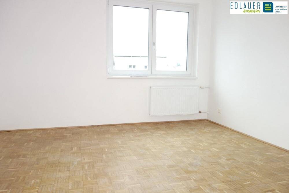 Heller, leerer Raum mit Parkettboden, weißen Wänden und Fenster mit Heizkörper.