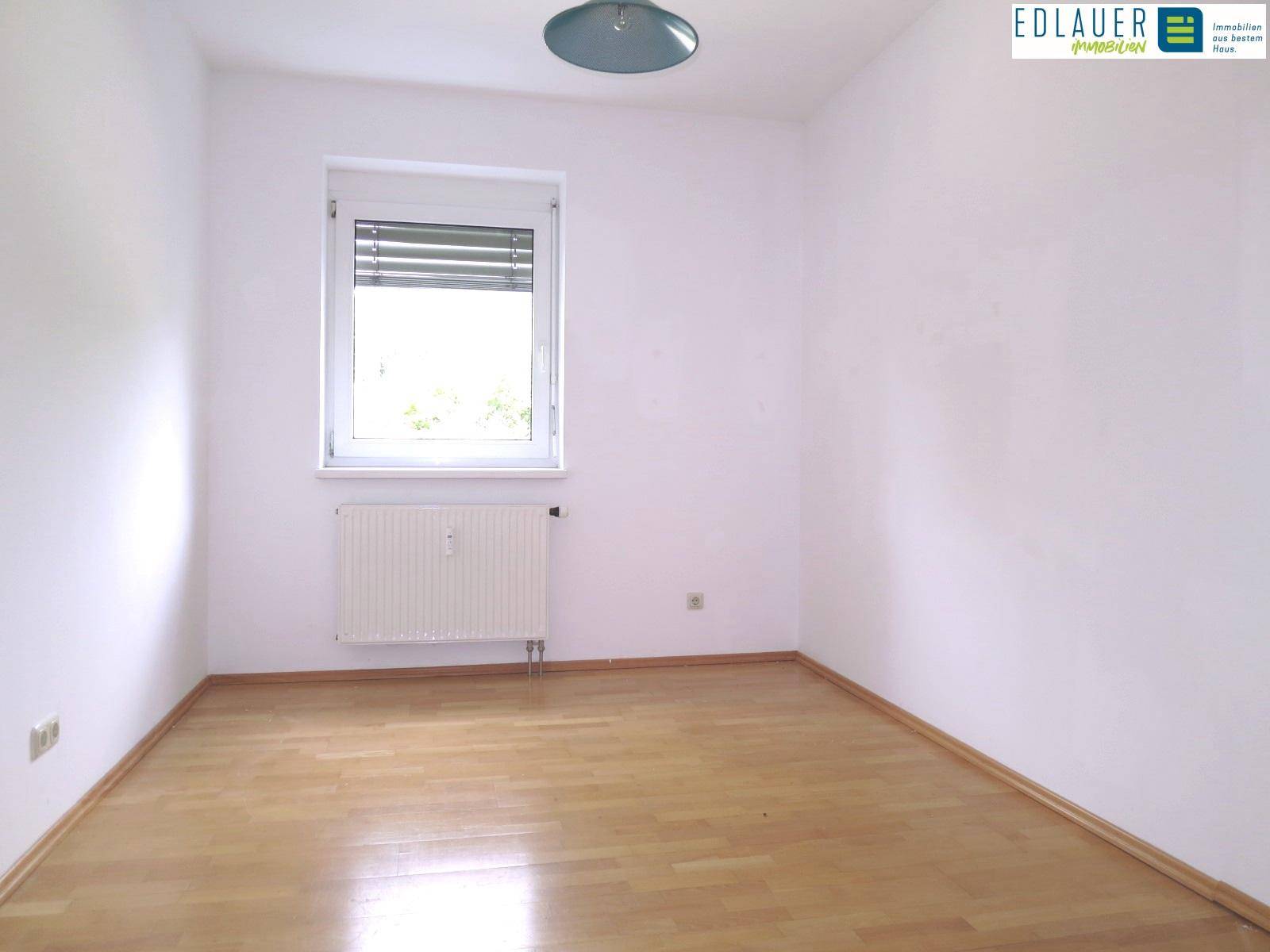 Helles Schlafzimmer mit Parkettboden und großem Fenster, bietet viel Tageslicht.