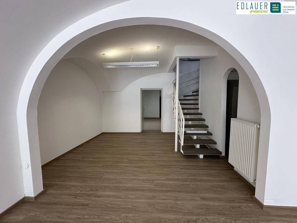 Heller Gewerberaum mit Holzboden, offenem Durchgang und einer Treppe zu einer oberen Ebene.