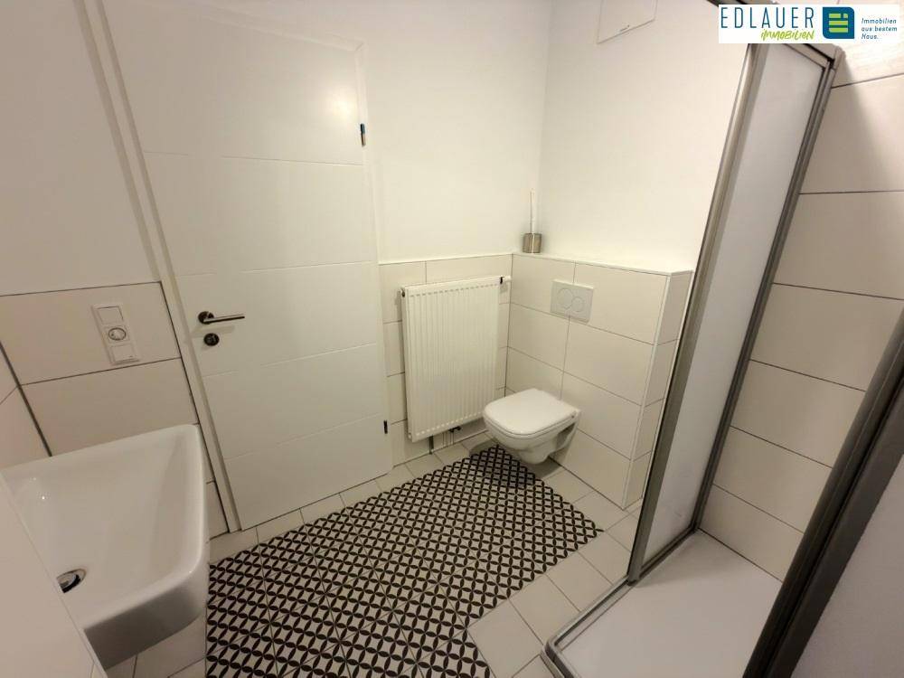 Modernes Badezimmer mit Duschkabine, WC und kleinem Waschbecken, ausgestattet mit weißen Fliesen.