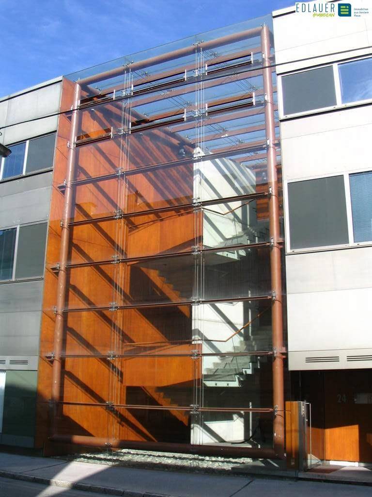 Vertikale Glasfassade mit Holzverkleidung, die ein Treppenhaus eines modernen Gebäudes umschließt.
