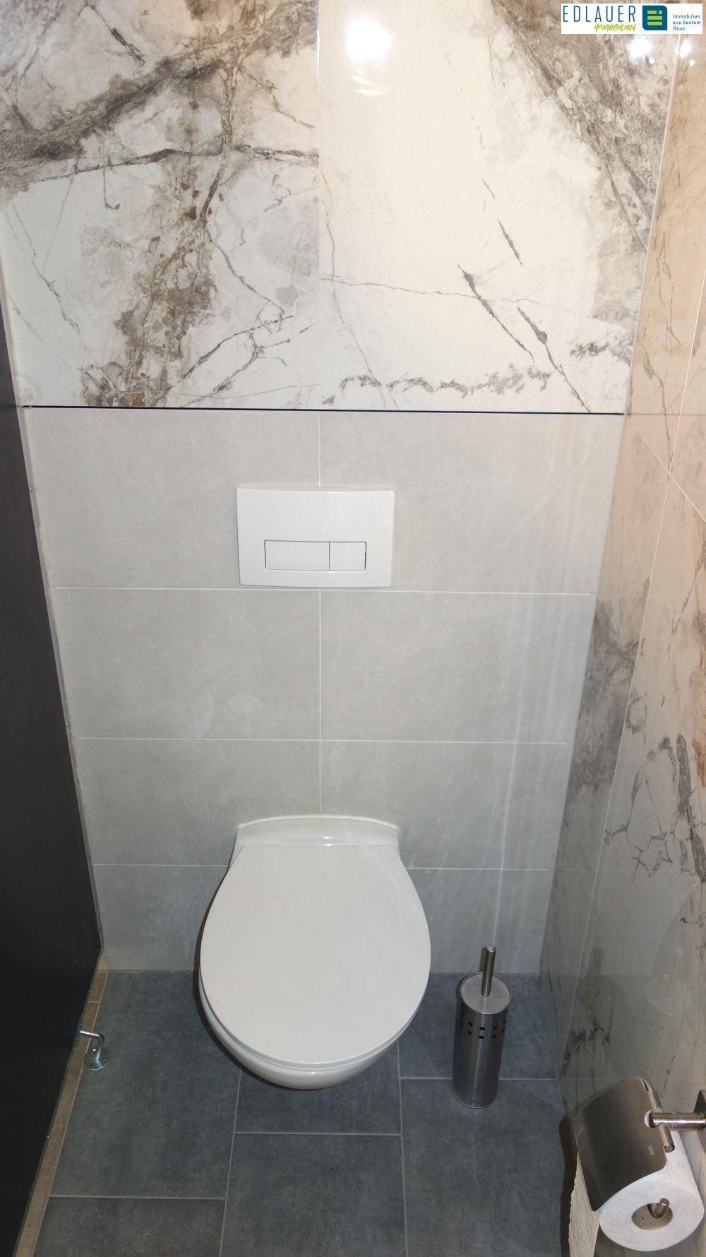 Badezimmer mit Wand-WC und Fliesen in zwei verschiedenen Mustern und Farben.