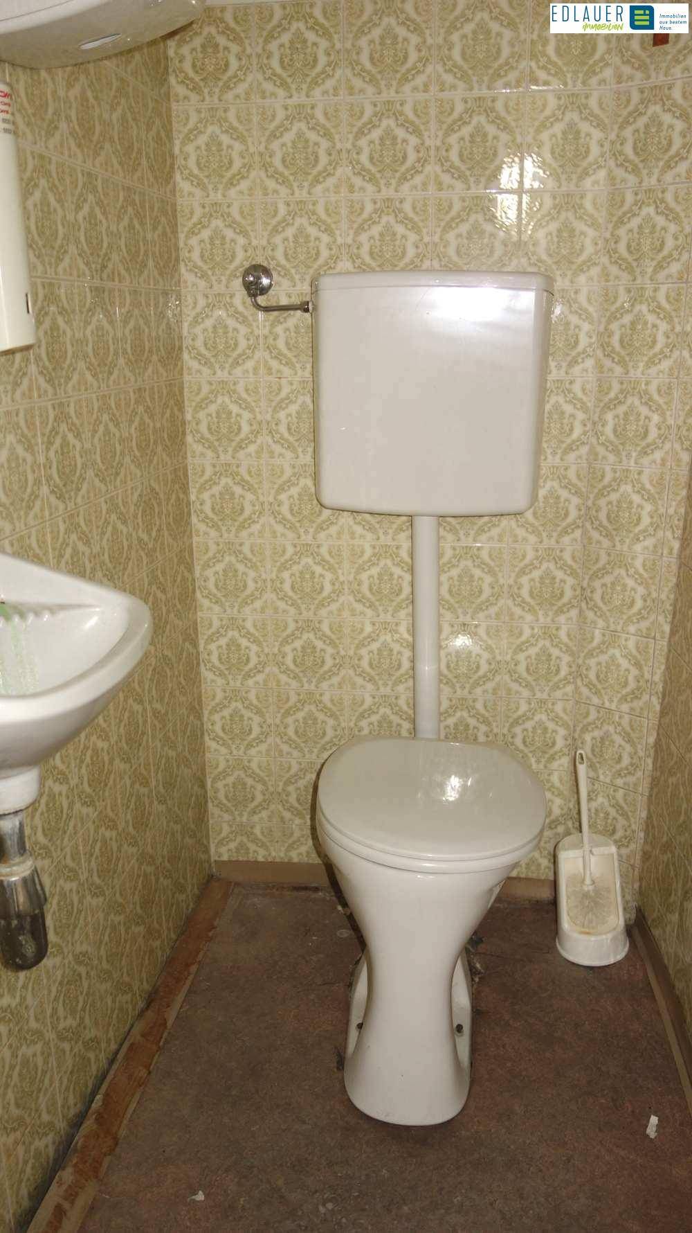 Toilette mit traditionellen gemusterten Fliesen an den Wänden und einem kleinen Waschbecken.