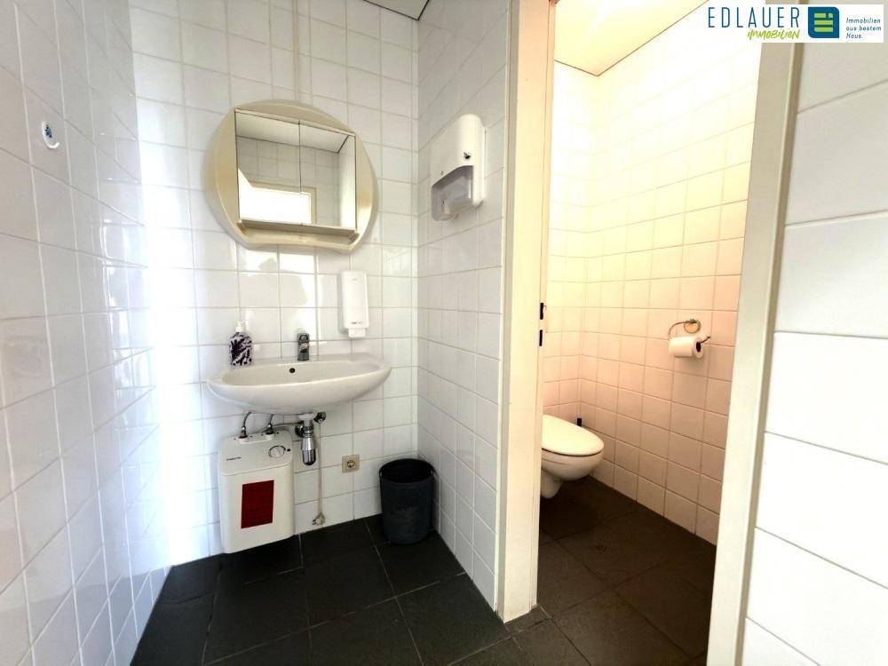 Gästetoilette mit weißen Fliesen, Waschbecken und Spiegel, sowie dunklem Fliesenboden.