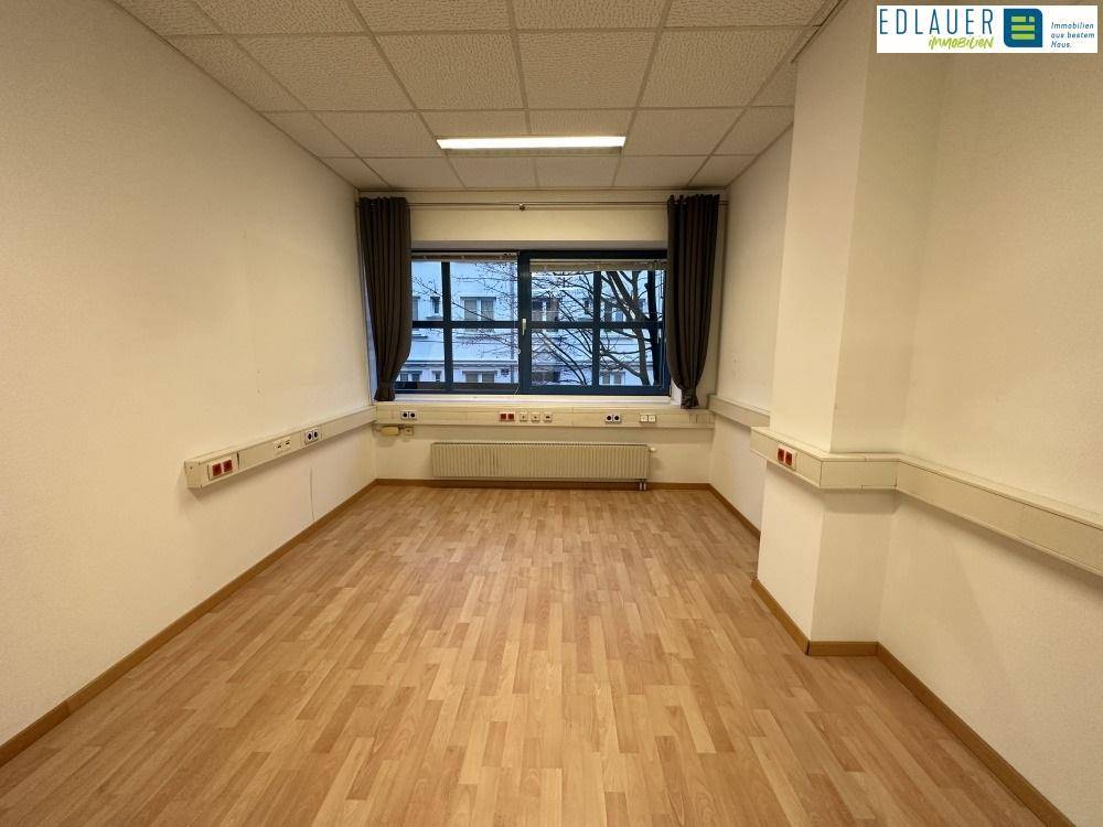 Großer Büroraum mit breiter Fensterfront, Laminatboden und weißen Wänden, bietet viel Tageslicht.