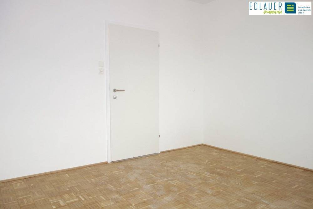 Leerer Raum mit Parkettboden, weißen Wänden und einer weißen Innentür.