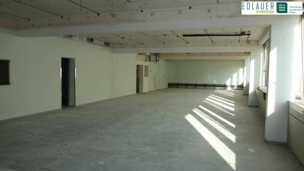 Sonnendurchfluteter Gewerberaum im Rohbau mit hohen Decken und großen Fenstern, die Streifen von Licht werfen.