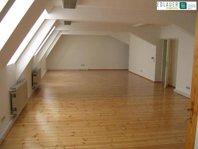 Geräumiger Dachbodenraum mit sichtbaren Holzbalken, schrägen Wänden und Dachfenstern, die viel natürliches Licht hereinlassen.