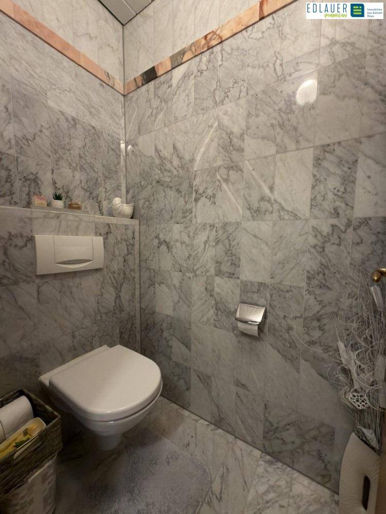 Separate Toilette mit Marmorfliesen und wandmontiertem WC.