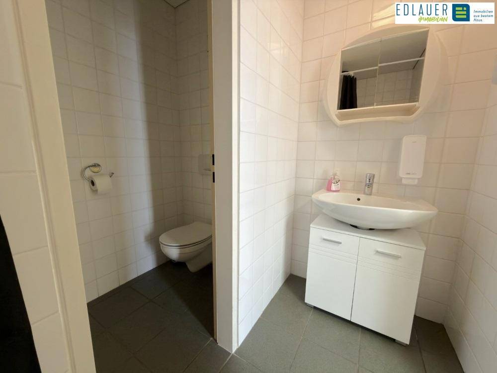 Gästetoilette mit weißen Fliesen, modernem Waschbecken und Spiegel, sowie dunklem Fliesenboden.