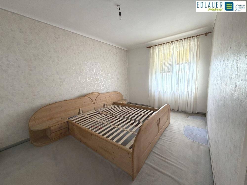 Schlafzimmer mit hellem Teppichboden und einem Holzbettgestell, bereit zur Einrichtung.