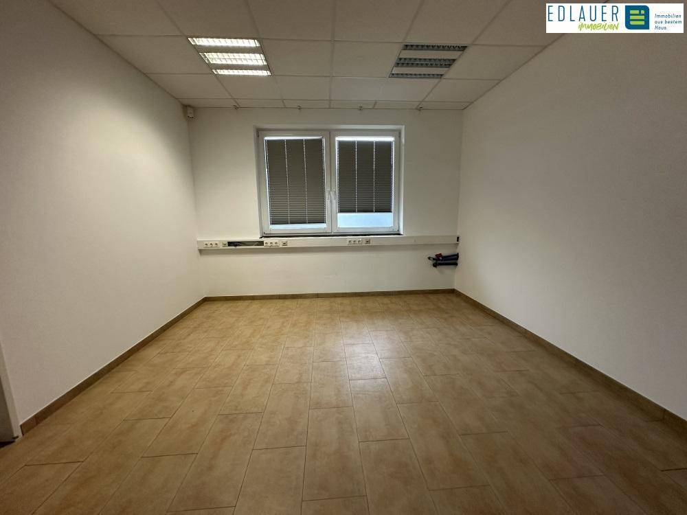 Leerer Büroraum mit Fliesenboden, großem Fenster und Deckenbeleuchtung, bietet vielseitige Nutzungsmöglichkeiten.