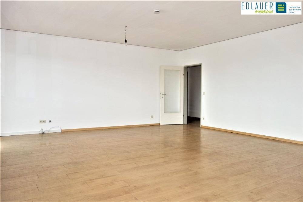 Geräumiges, leeres Wohnzimmer mit hellem Parkettboden und weiß gestrichenen Wänden.