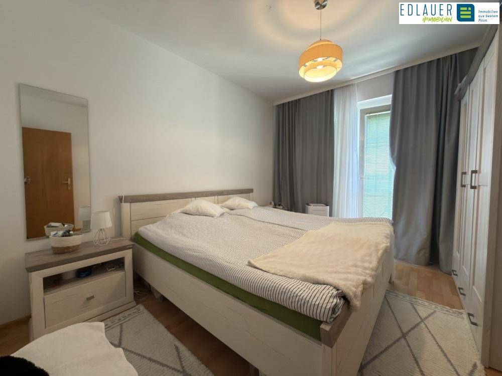Helles Schlafzimmer mit Doppelbett, Holzmöbeln und Zugang zu einem Balkon.