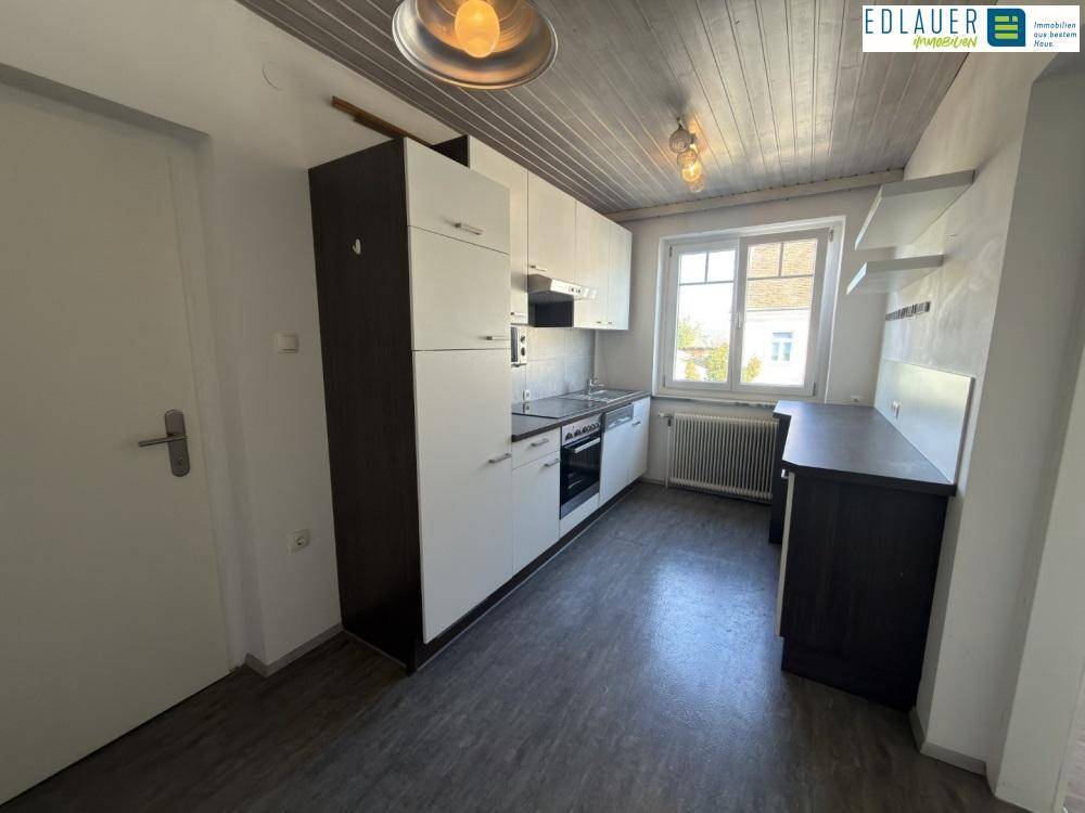 Helle Küche mit Fenster, weißen Oberschränken und dunkler Arbeitsplatte.