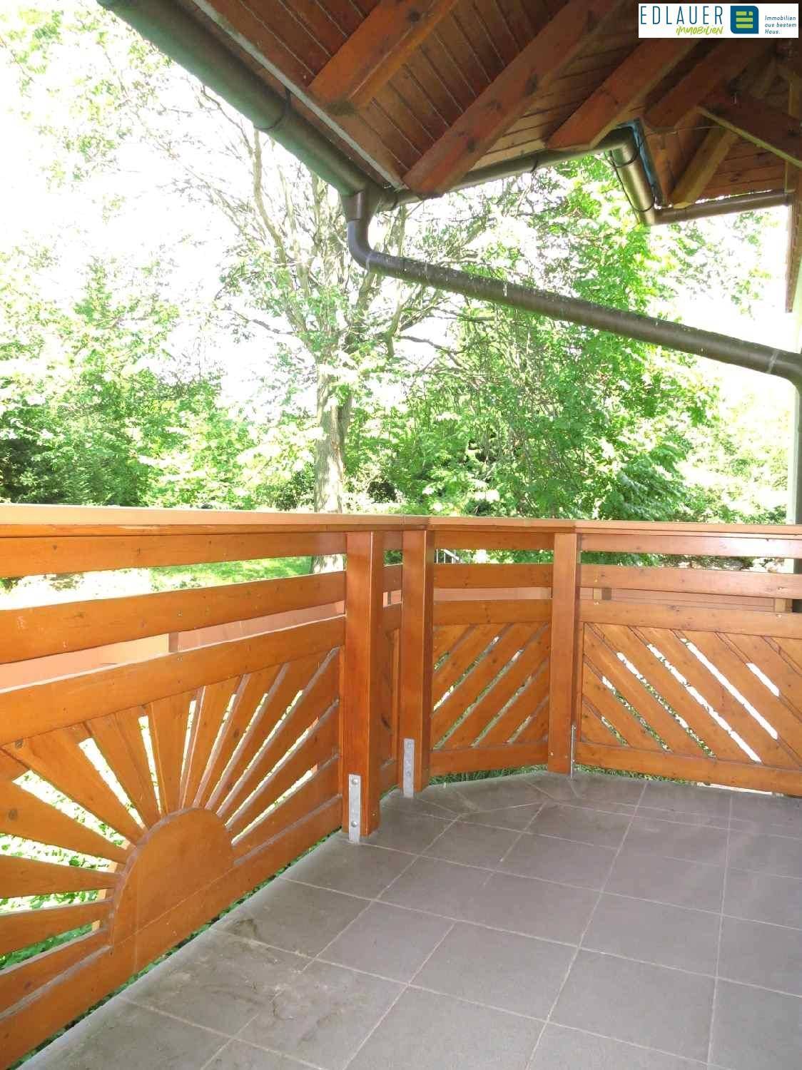 Gemütlicher Holzbalkon mit Fliesenboden und schöner Aussicht ins Grüne.