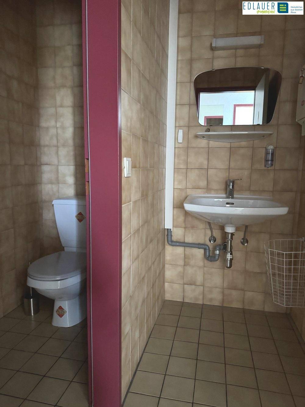 Toilette mit beigefarbenen Fliesen, Waschbecken und WC, in einem gut gepflegten Zustand.