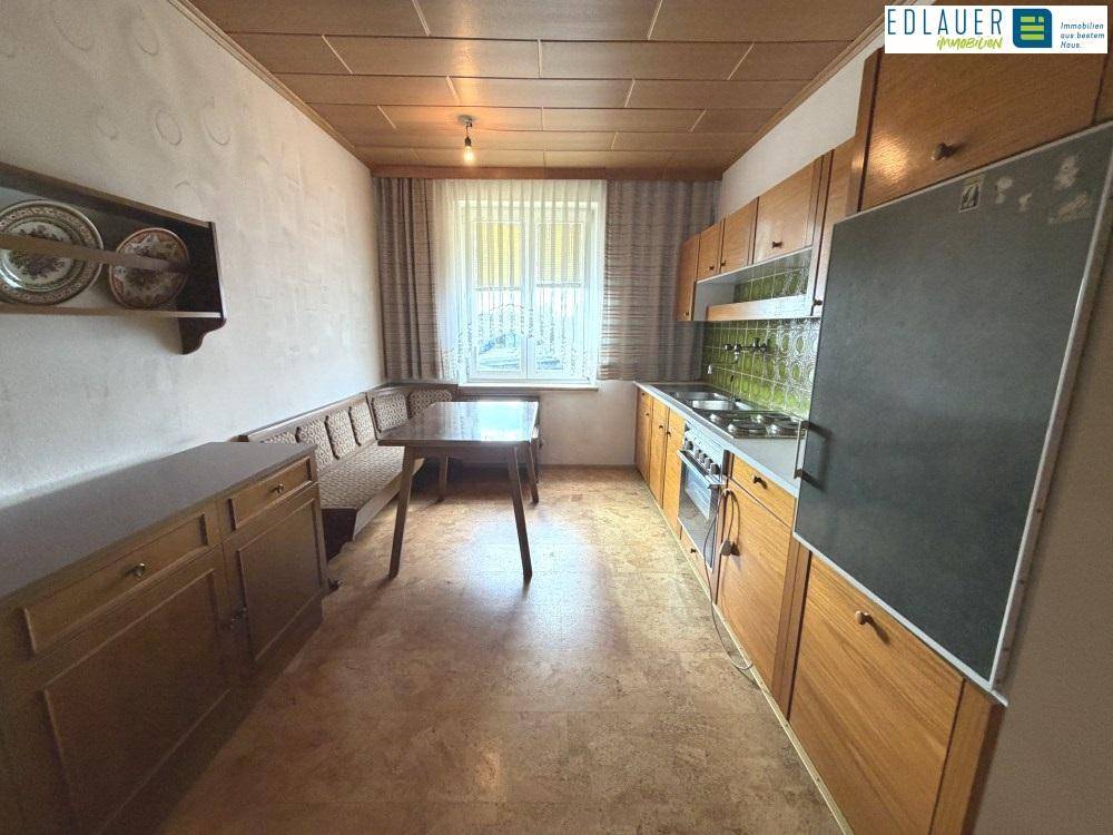 Gemütliche Wohnküche mit Holzdecke, Einbauküche und Essbereich am Fenster.