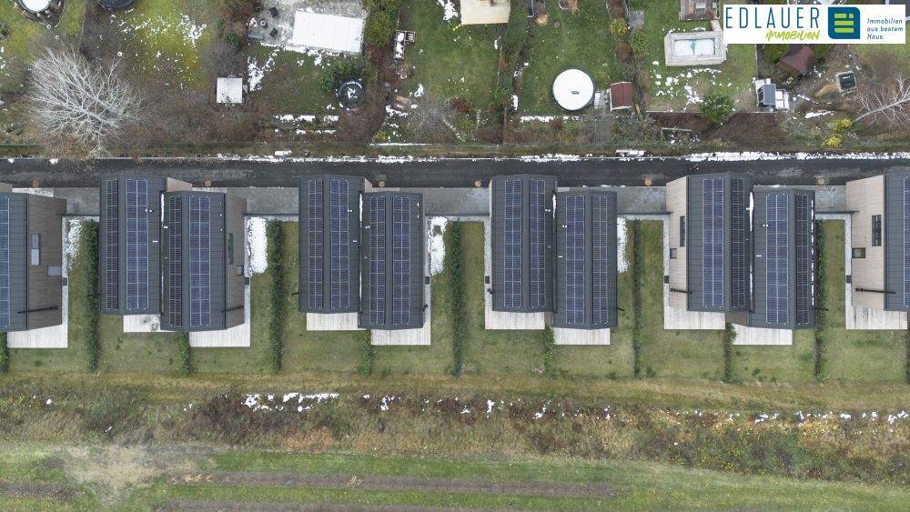 Luftaufnahme einer Reihe von Häusern mit Photovoltaikanlagen auf den Dächern und Gärten.