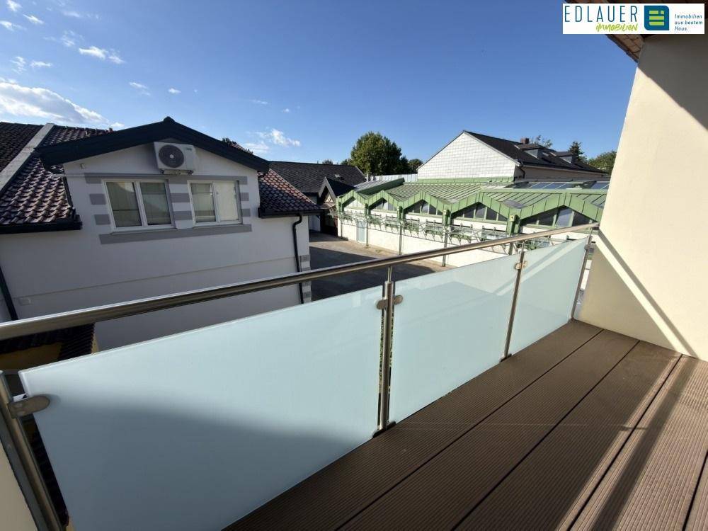 Balkon mit modernen Glasgeländern und Holzdielenboden, bietet Blick auf umliegende Gebäude.