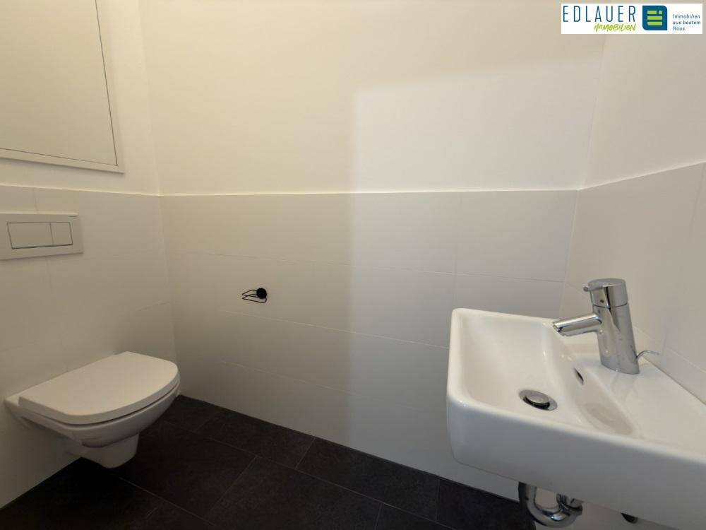 Separates Gäste-WC mit Wand-WC und kleinem Waschbecken, ausgestattet mit dunklen Bodenfliesen.