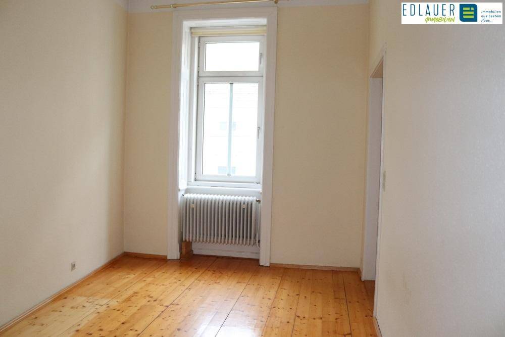 Gemütliches Zimmer mit Holzdielenboden und einem hohen Fenster, das für ausreichend Helligkeit sorgt.