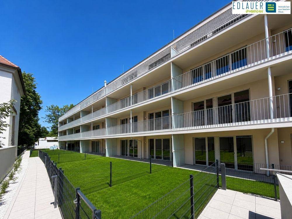 Modernes Mehrfamilienhaus mit Balkonen, Terrassen und begrünten Außenbereichen unter blauem Himmel.