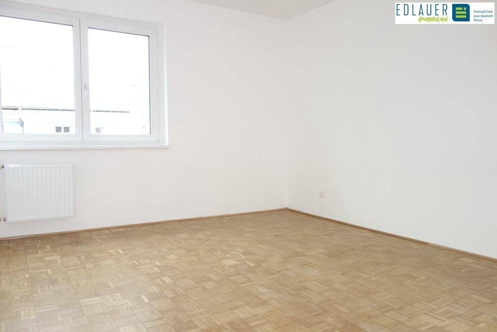 Heller, leerer Raum mit Parkettboden, weißen Wänden und großem Fenster.