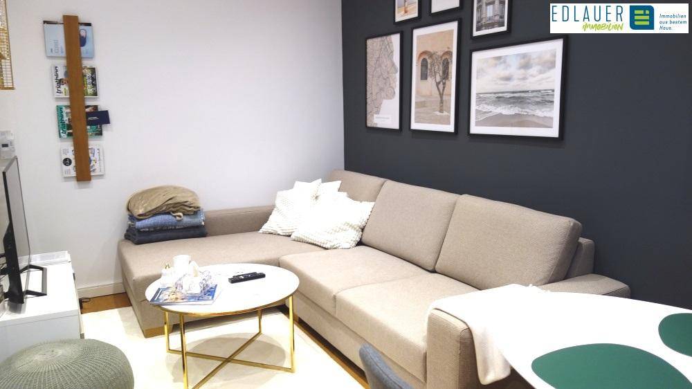 Gemütliches Wohnzimmer mit beigem Ecksofa, dunkler Akzentwand und modernen Bildern.