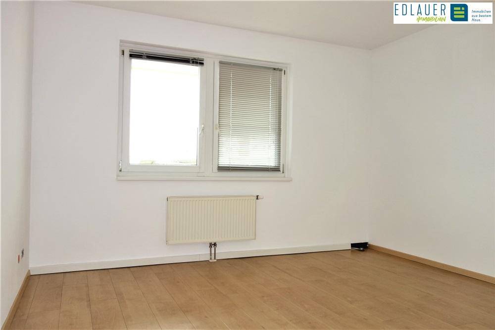 Helles Schlafzimmer mit Parkettboden, einem Fenster mit Jalousien und Heizkörper.