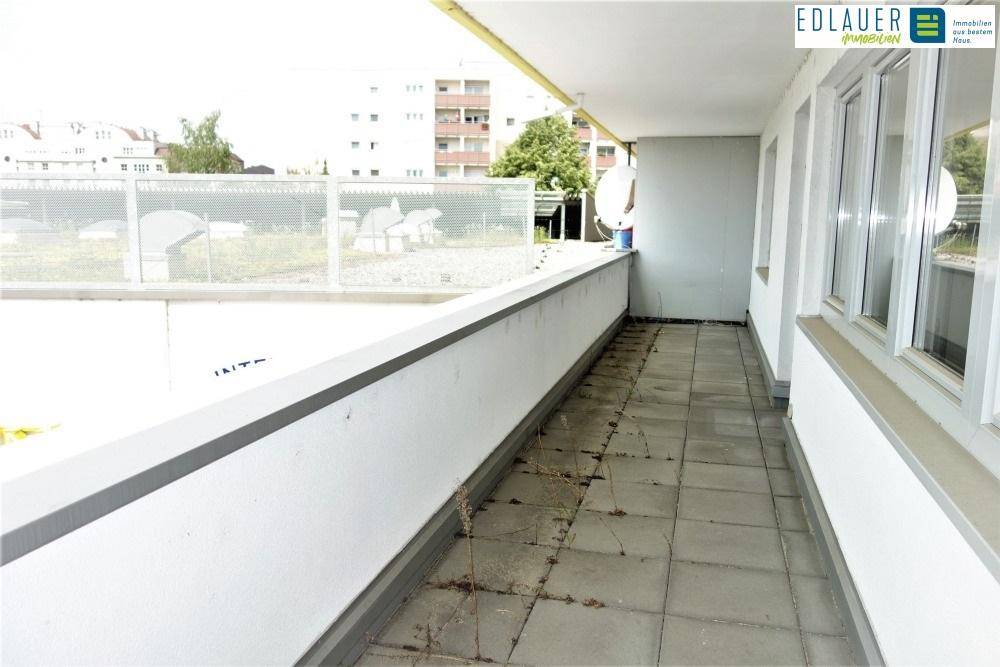 Geräumiger Balkon mit Fliesen und Metallgeländer, teilweise mit Bewuchs und Satellitenschüsseln.