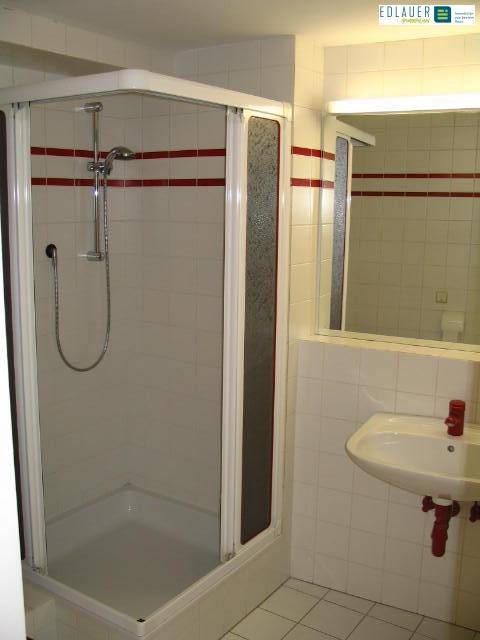 Badezimmer mit Duschkabine, Waschbecken und weiß gefliesten Wänden, akzentuiert durch rote Streifen für einen modernen Touch.