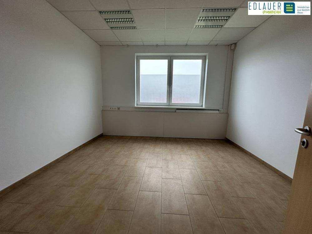 Sauberer Büroraum mit Fliesenboden, Fenster und weiß gestrichenen Wänden, bietet eine neutrale Arbeitsatmosphäre.