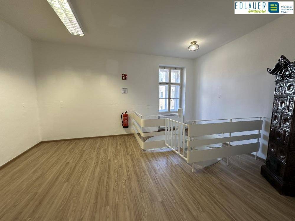 Raum mit Laminatboden, Fenster, Geländer und einem traditionellen Kachelofen, der Charakter verleiht.