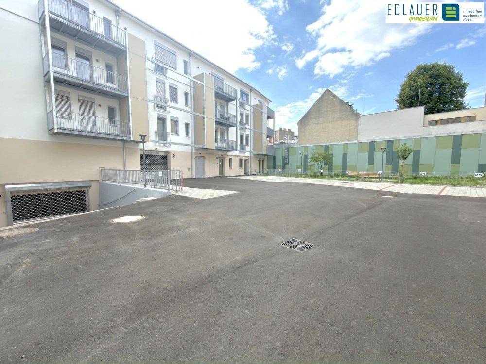 Ansicht des modernen Wohnkomplexes mit Tiefgaragenzufahrt und Außenparkplätzen.
