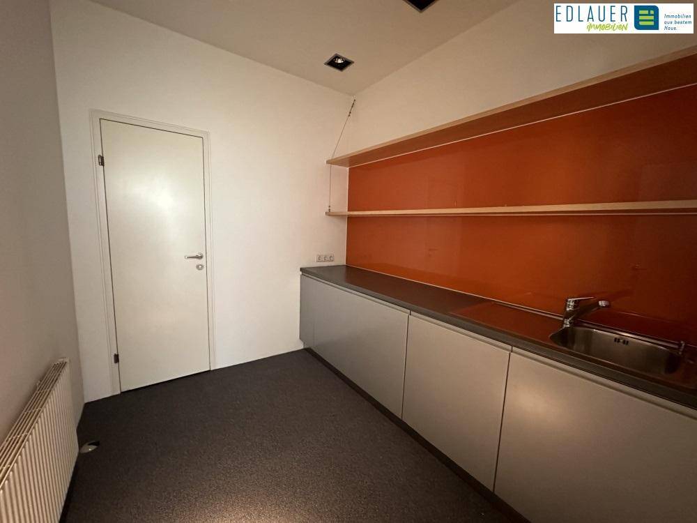 Kleine Küchenzeile mit Spüle, Unterschränken und offenen Regalen vor einer orangefarbenen Rückwand.