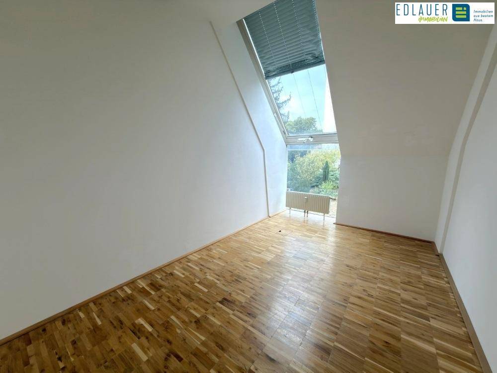 Büroraum mit Holzparkettboden, weißen Wänden und einem großen Dachfenster mit Blick ins Grüne.