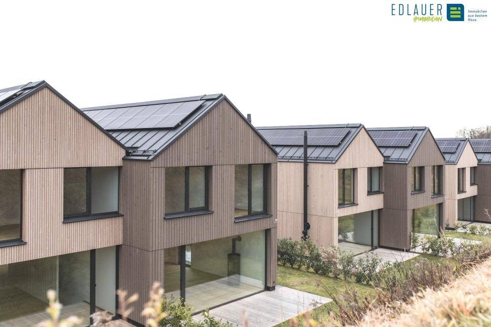 Nahaufnahme moderner Reihenhäuser mit Holzfassaden, großen Fenstern und Solarmodulen auf den Dächern.