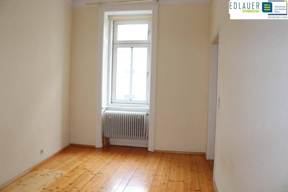 Helles Zimmer mit Holzdielenboden und einem großen Fenster, das viel Licht hereinlässt.