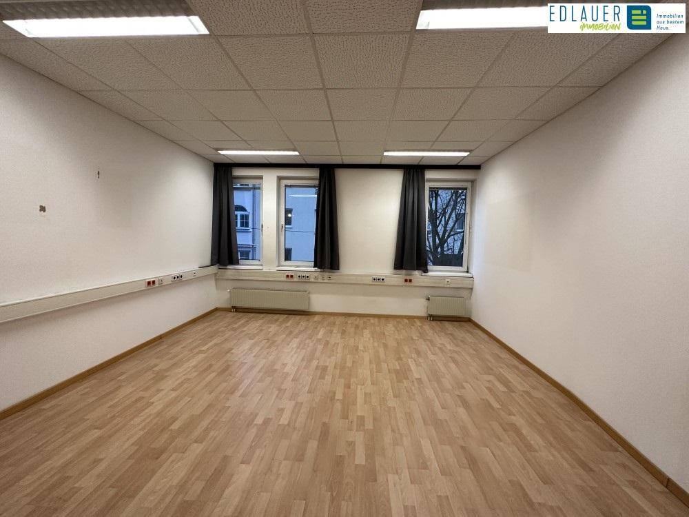 Heller Büroraum mit Laminatboden und Fensterfront, ausgestattet mit Deckenleuchten und Wandsteckdosen.